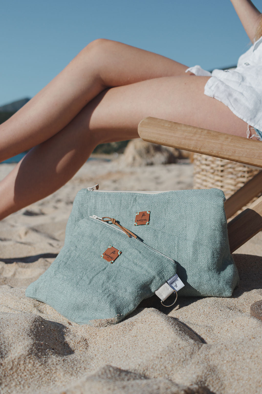 Cosmetic bag pouch made with linen with summer essentials and a coin purse near a woman in a chair at the beach 