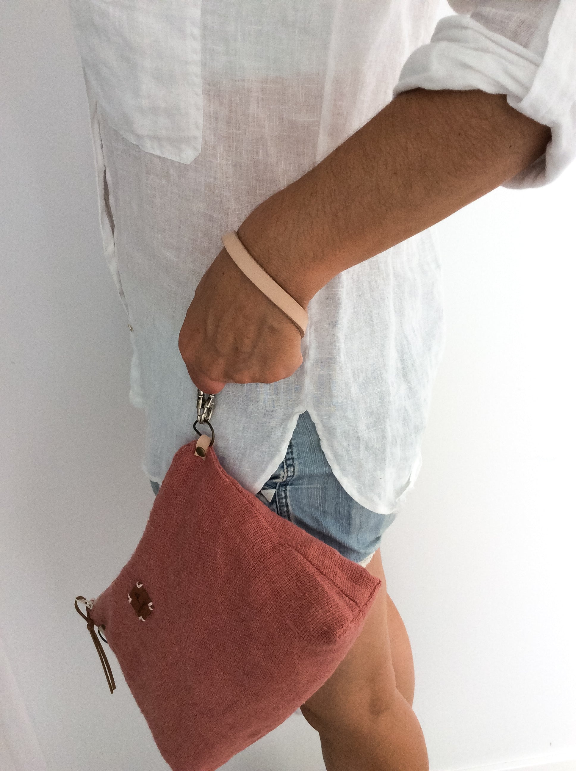 woman wearing a white linen shirt and a linen slouchy pouch in rose with a thin leather strap in her wrist