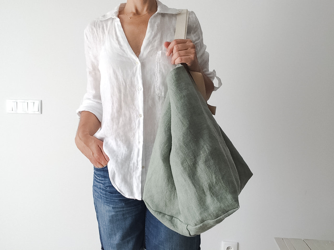 woman wearing a white linen shirt and a big beach linen bag in green