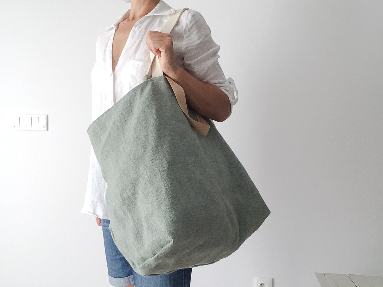 woman wearing a white linen shirt and a big beach linen bag in green