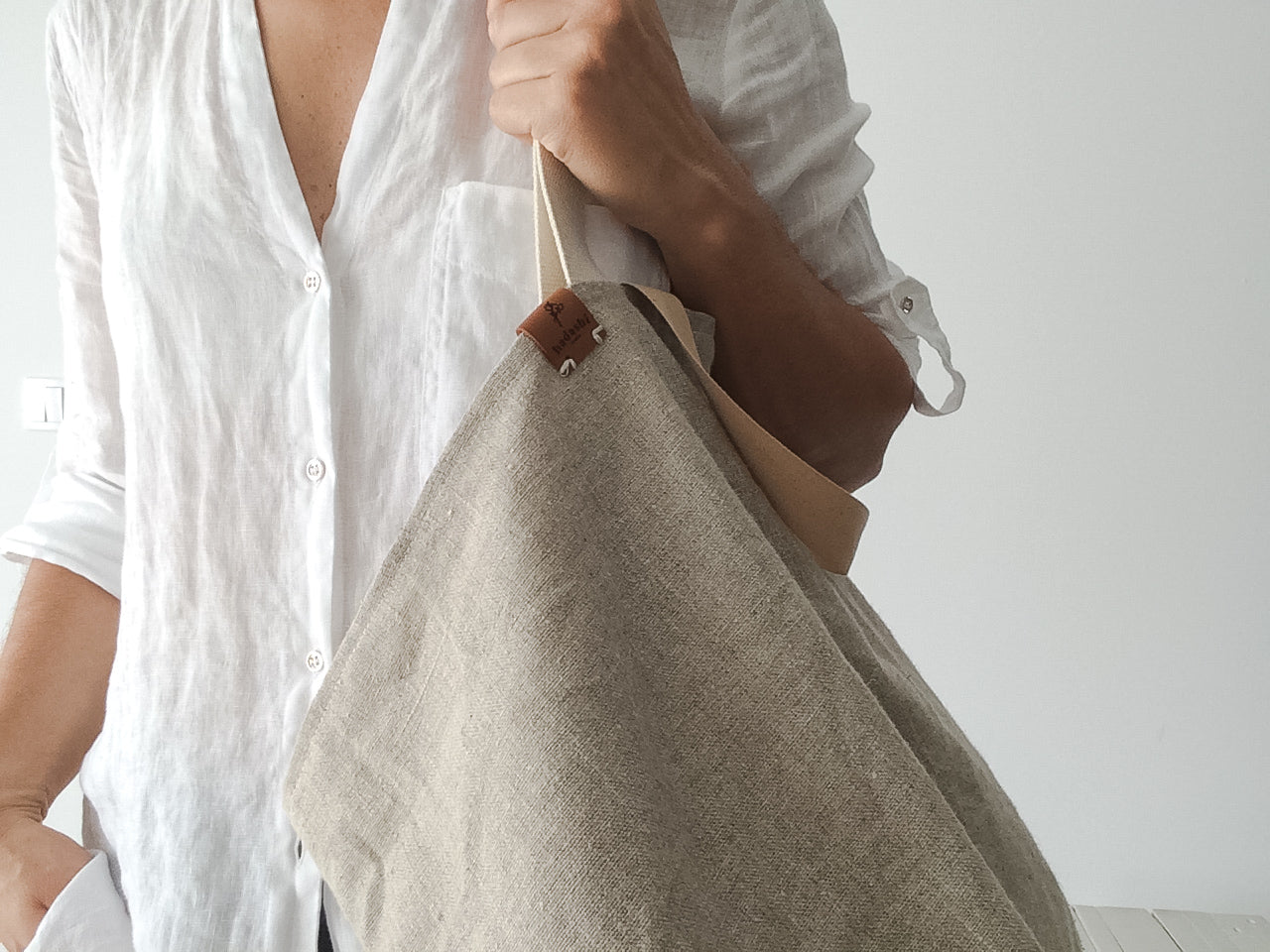 woman wearing a white linen shirt and a big beach linen bag in natural color