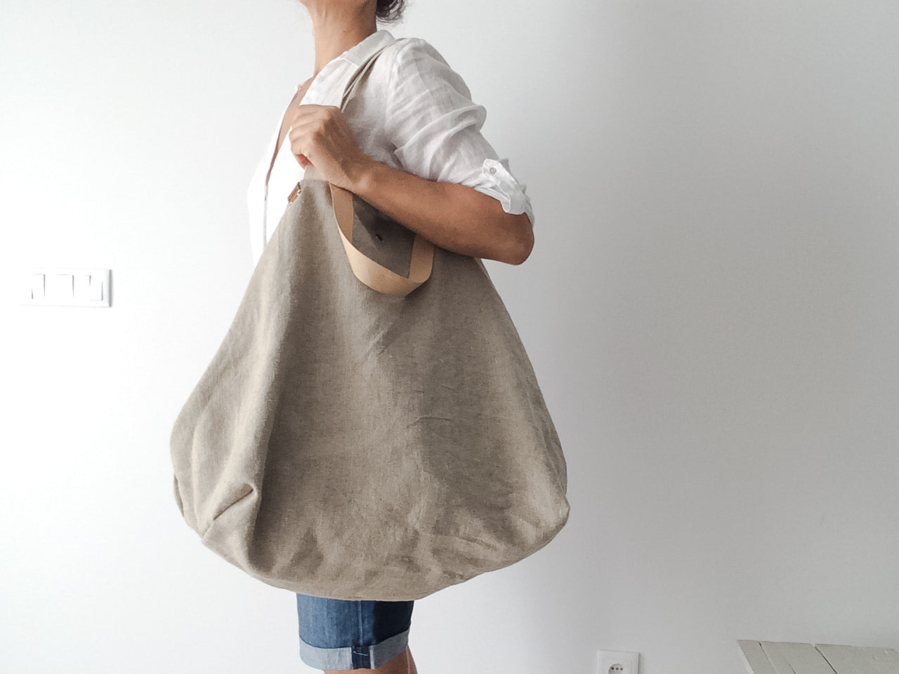 woman wearing a white linen shirt and a big beach linen bag in natural color