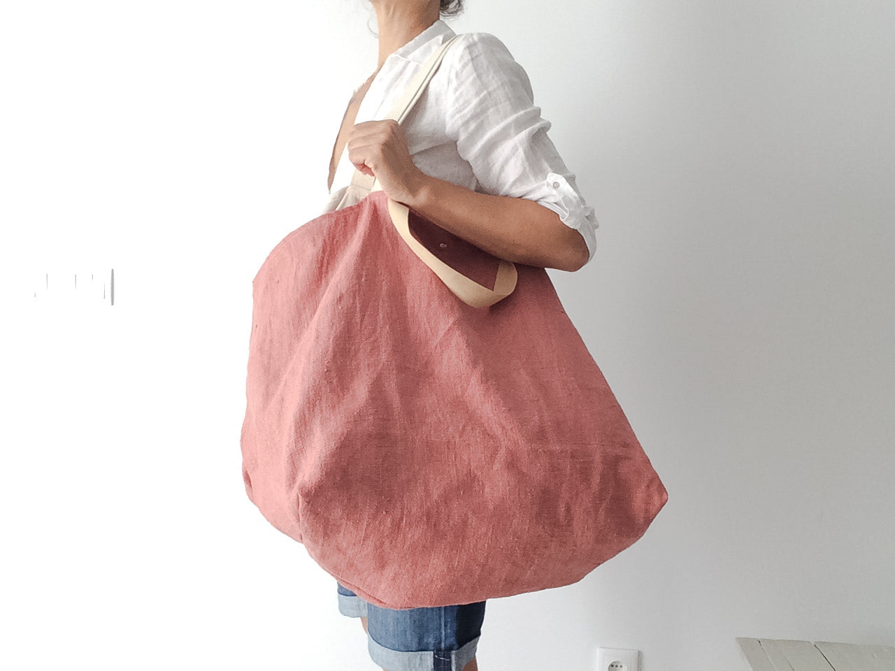 woman wearing a white linen shirt and a big beach linen bag in rose color