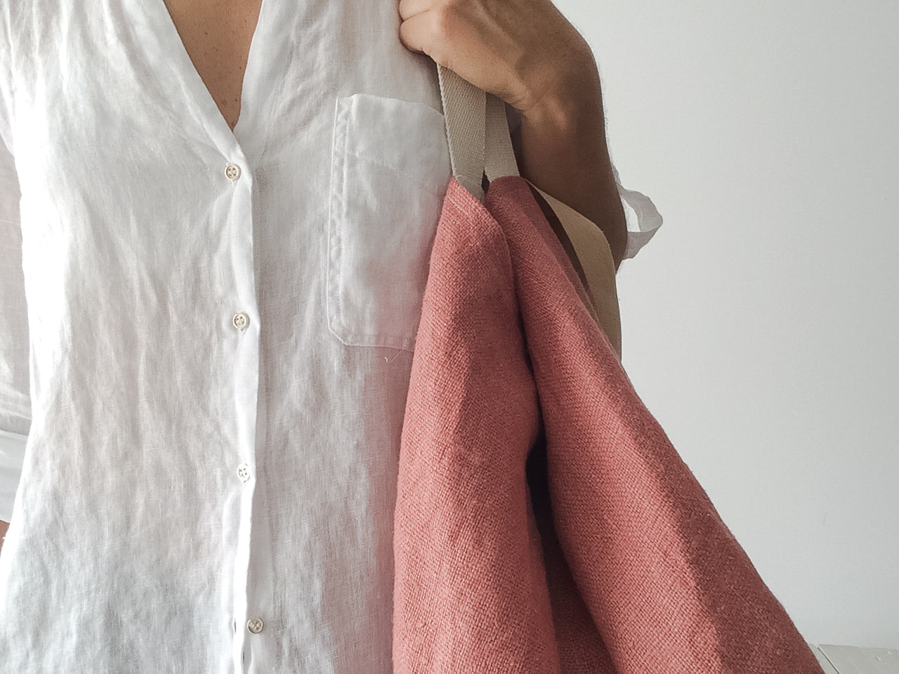 woman wearing a white linen shirt and a big beach linen bag in rose color