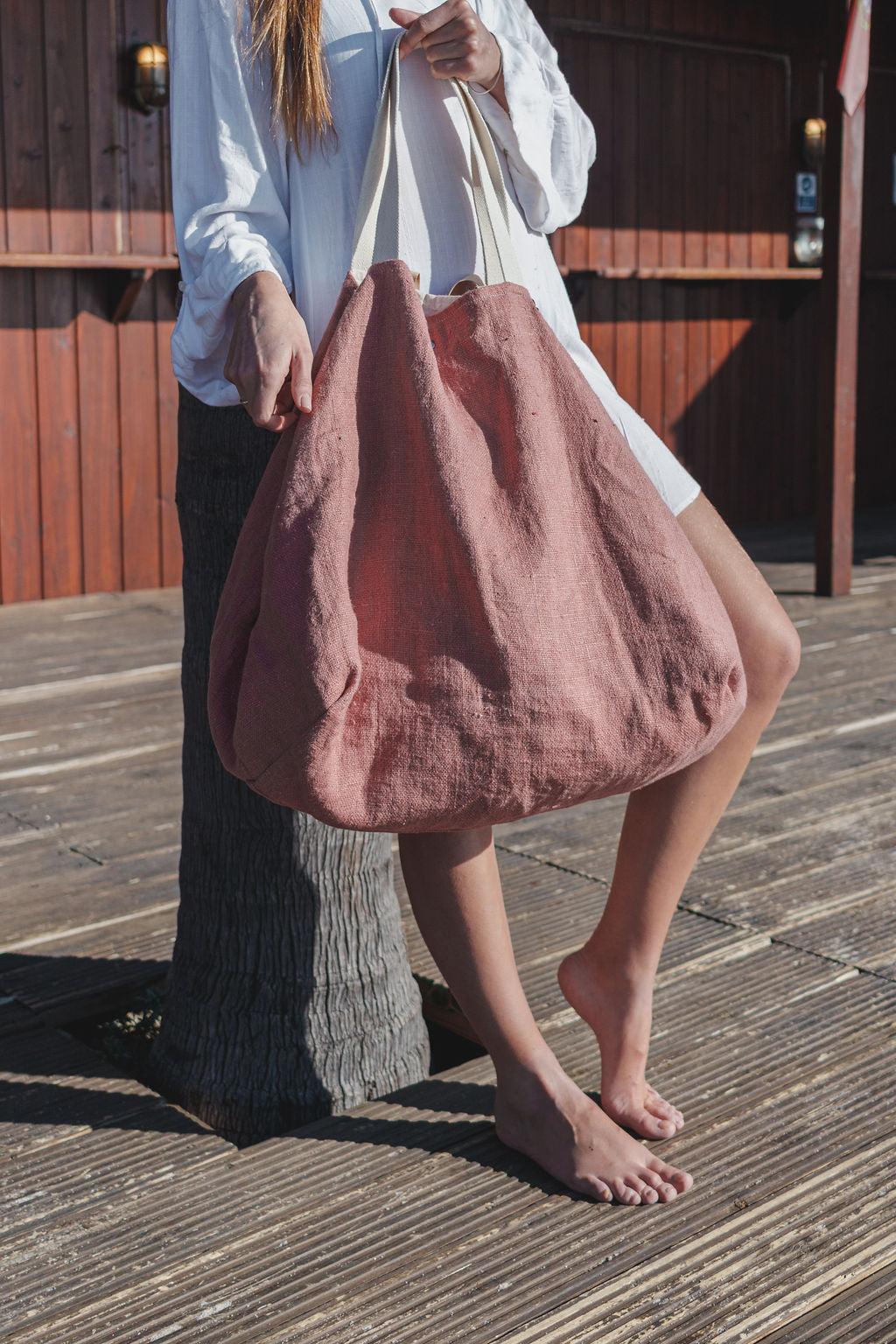 woman at the beach wearing a white linen shirt and a big beach linen bag in rose color